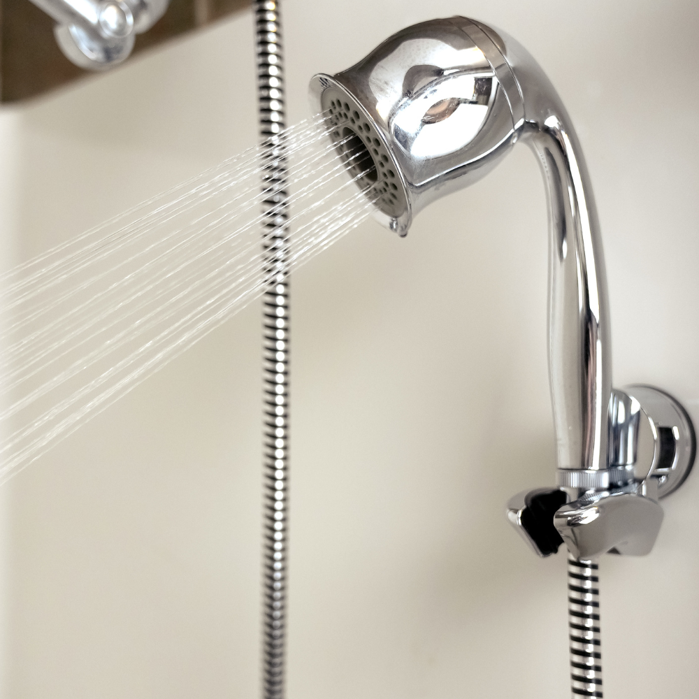 Close-up of a chrome handheld shower head spraying water, attached to a flexible hose. The setting is simple and clean, conveying freshness.