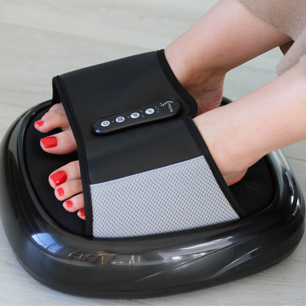 A close-up of a foot massager with a person's foot and bright red toenails resting inside, showcasing control buttons on the device.