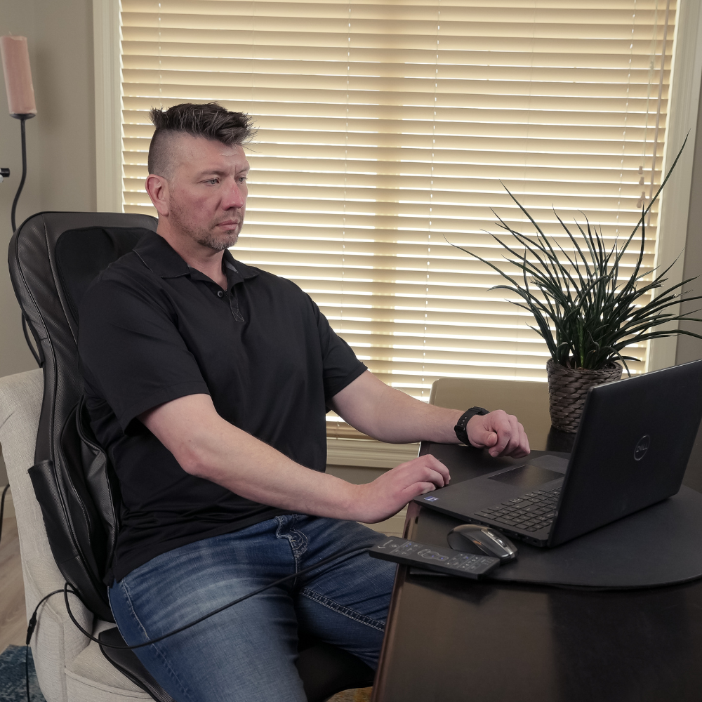 A man working while sitting on a Shiatsu Neck and Back Massager With Air Compression Chair Cushion Chair.