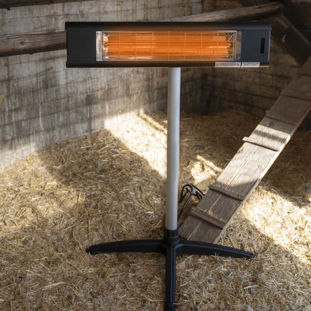 Infrared Heater on a stand in a barn setting with wooden walls and straw flooring.