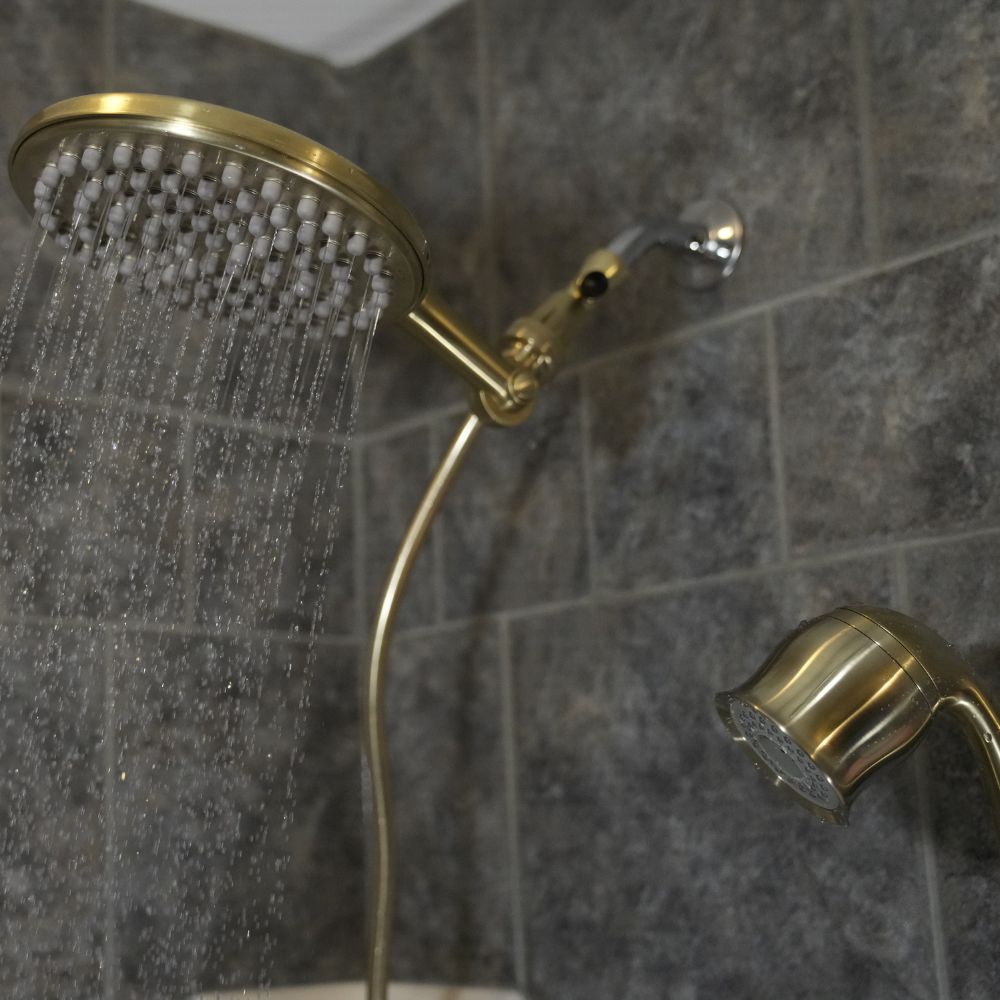 Gold shower head and handheld shower on a tiled wall