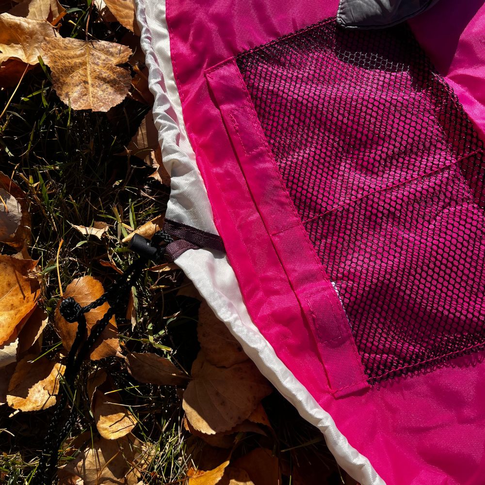 Close-up of a pink and white Nifty Sac Toy Organizer on grass with leaves.