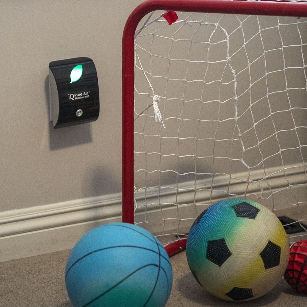 Children's sports balls near a small basketball hoop with an air purifier on the wall.