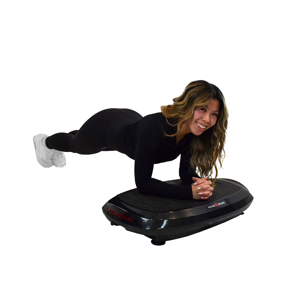 A person in black athletic wear performs a plank position on a vibration plate, showcasing a fitness workout setting.