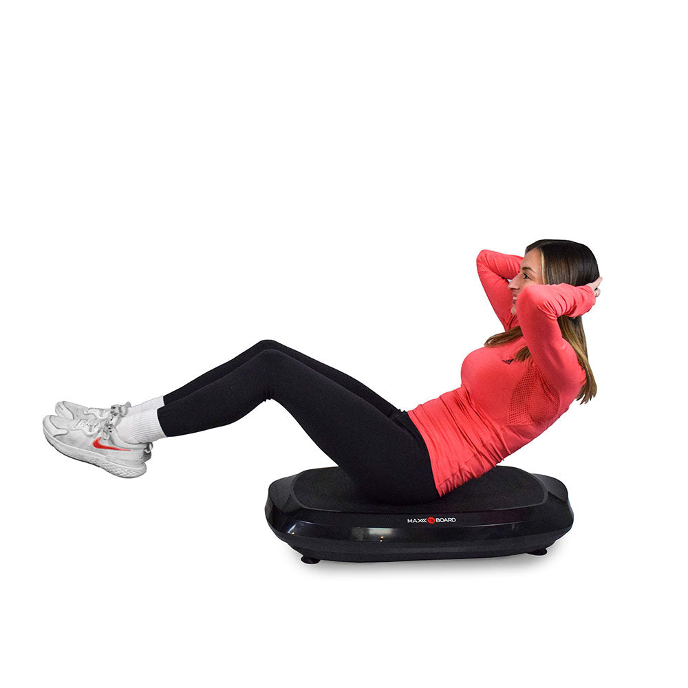 A person performs situps on a fitness balance board, wearing a pink long-sleeve shirt and black leggings.