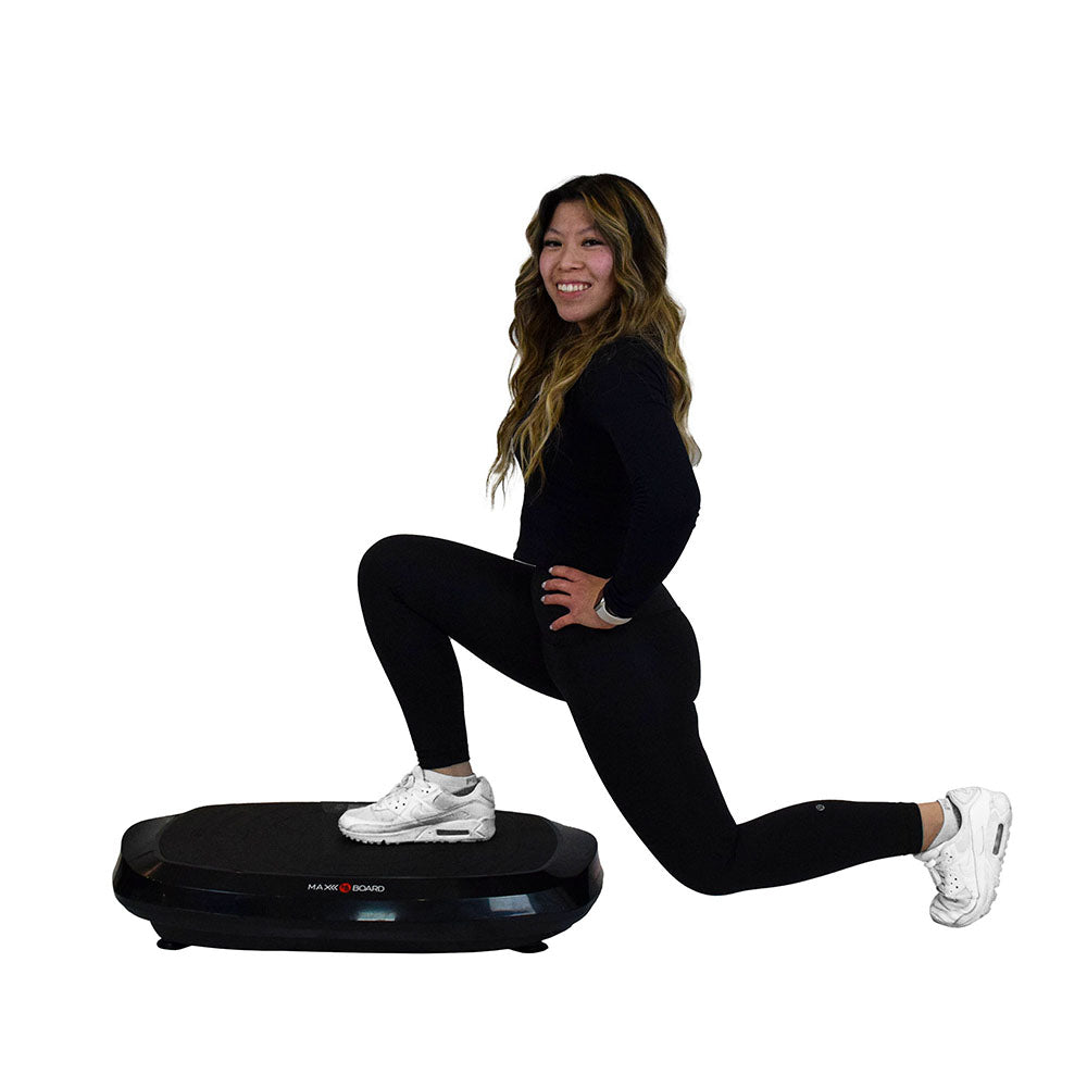 A person in black athletic wear performs a step position on a vibration plate, showcasing a fitness workout setting.