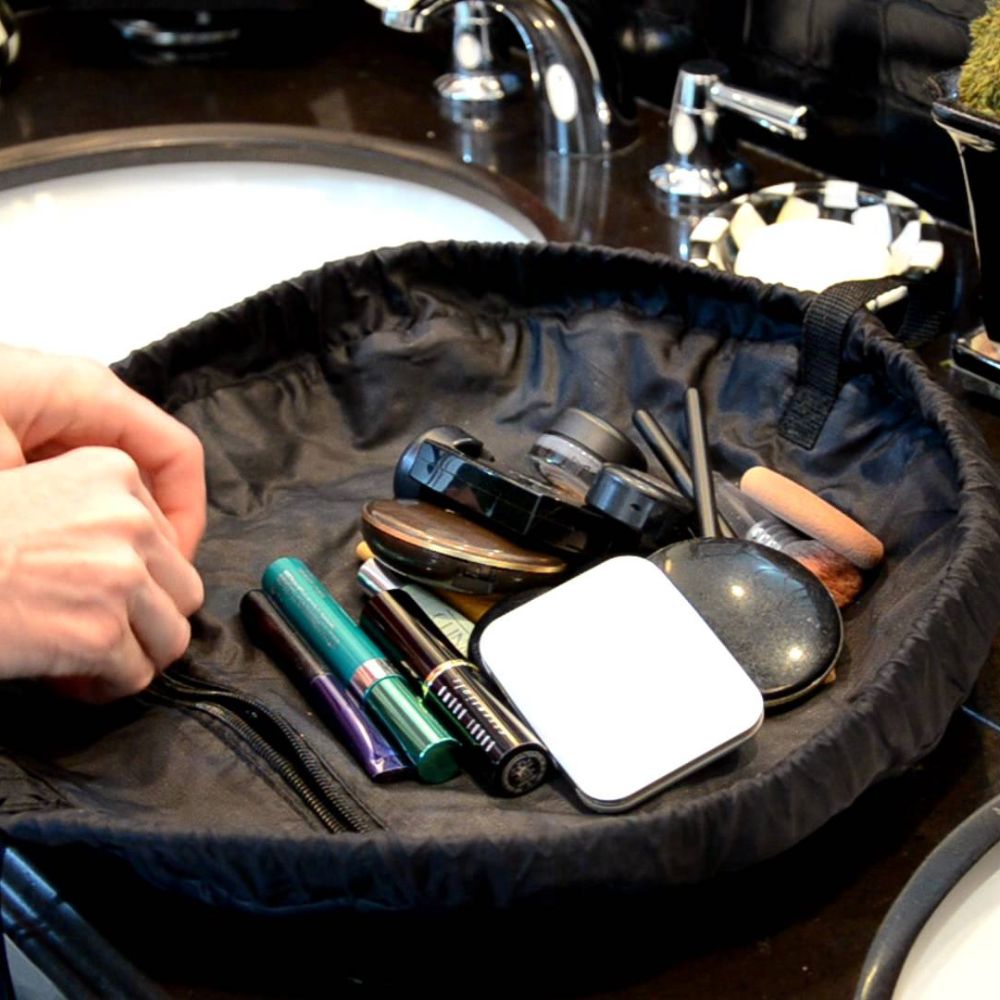 Black makeup bag with cosmetic items on a bathroom counter