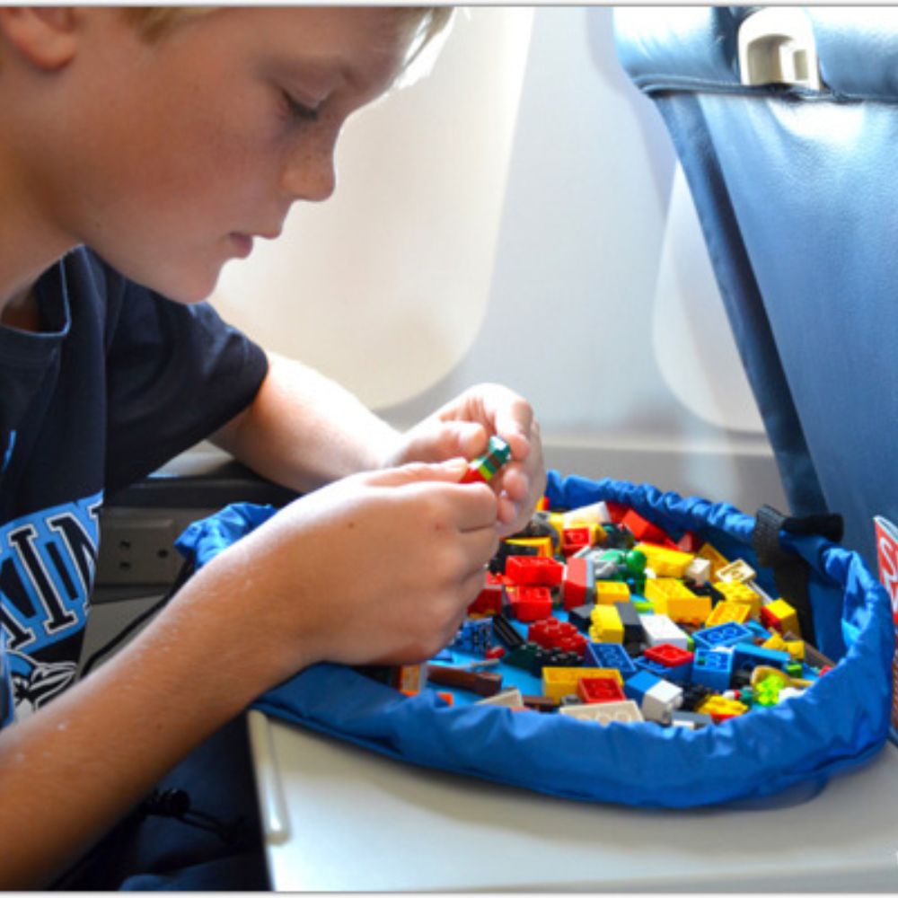 Child playing with colorful building blocks on a blue organizer inside an airplane.