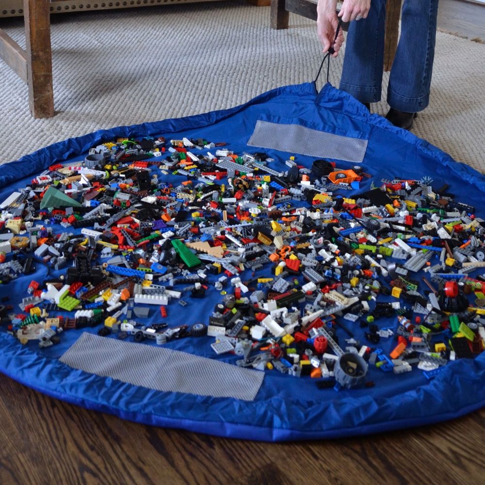 Blue Nifty Sac toy storage mat filled with colorful building blocks on a wooden floor.
