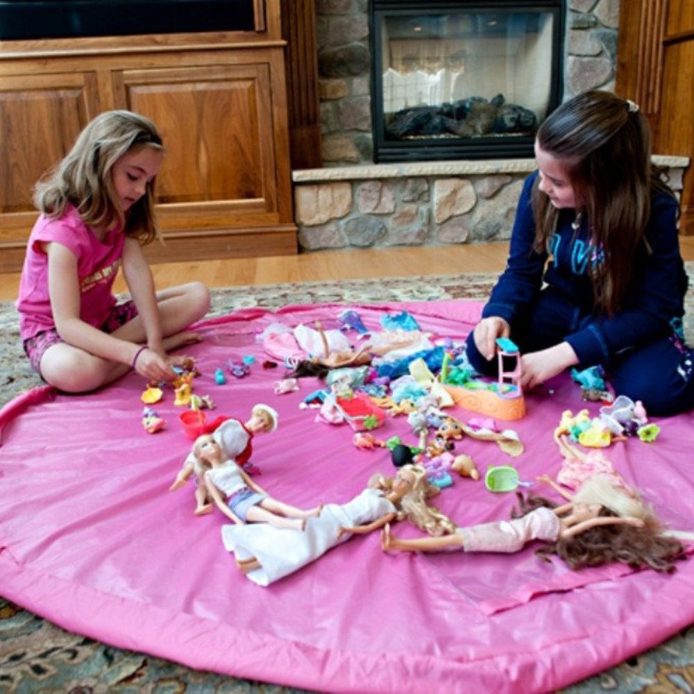 Two children playing with dolls and toys on a pink Nifty Sac in a living room.