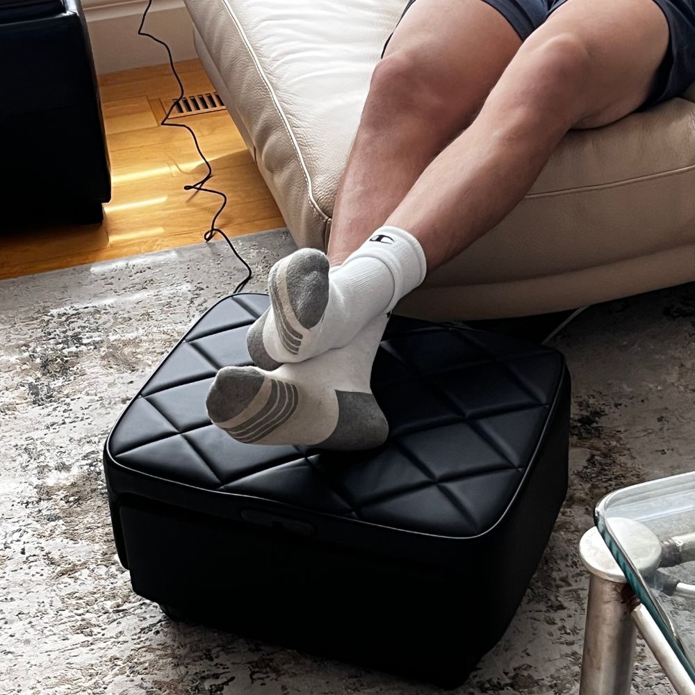 Person with feet up on a black massage ottoman, wearing white socks with gray accents.