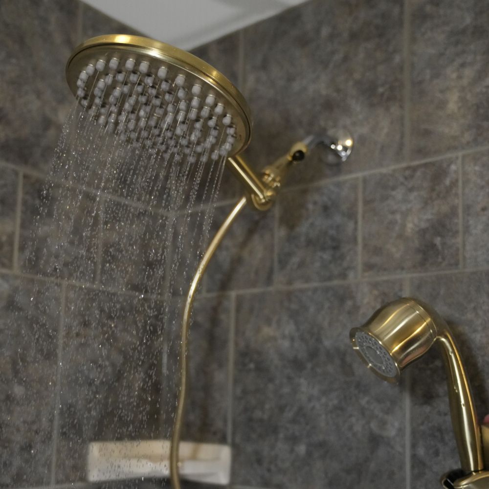 Gold shower head and handheld shower on a dark tiled bathroom wall